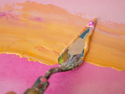 A Person Painting A Pink Wall With Yellow Paint