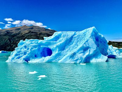 An Iceberg Floats On Blue Waters Under A Bright Sky