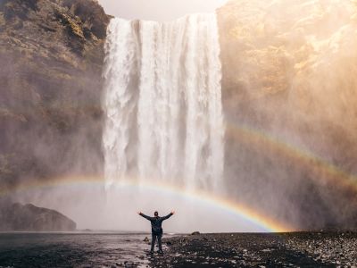Person In Front Of Waterfalls With Double Rainbow During
