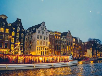 Boat Sailing On River Near Lighted Houses And Trees
